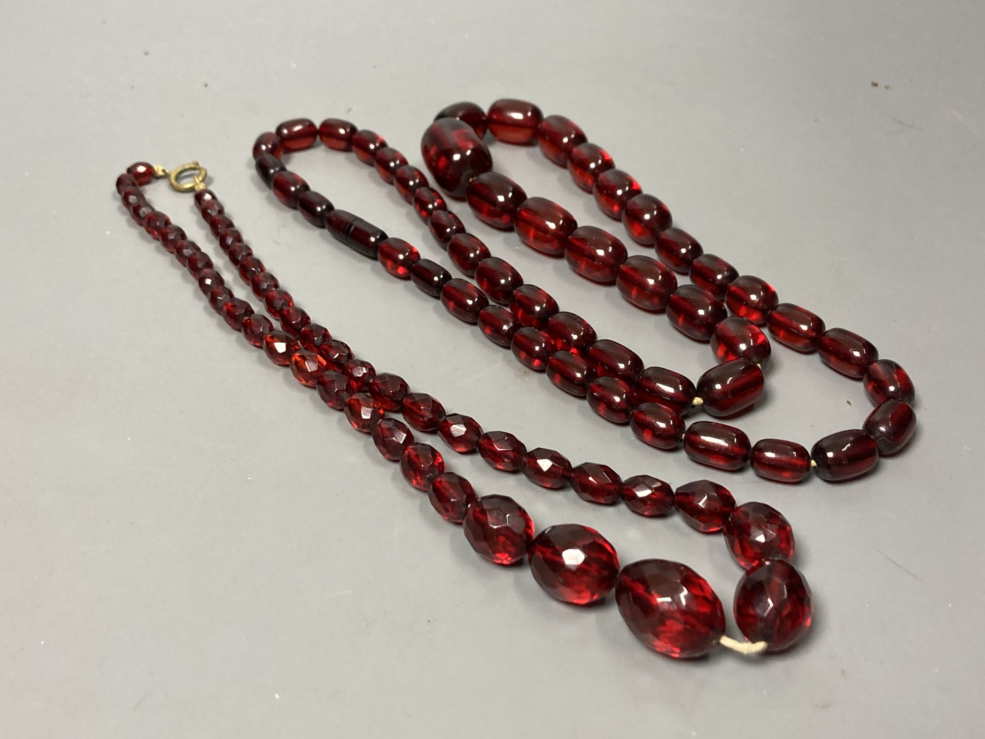 Two transluscent single strand simulated cherry amber bead necklaces, longest 82cm, gross weight 120 grams.